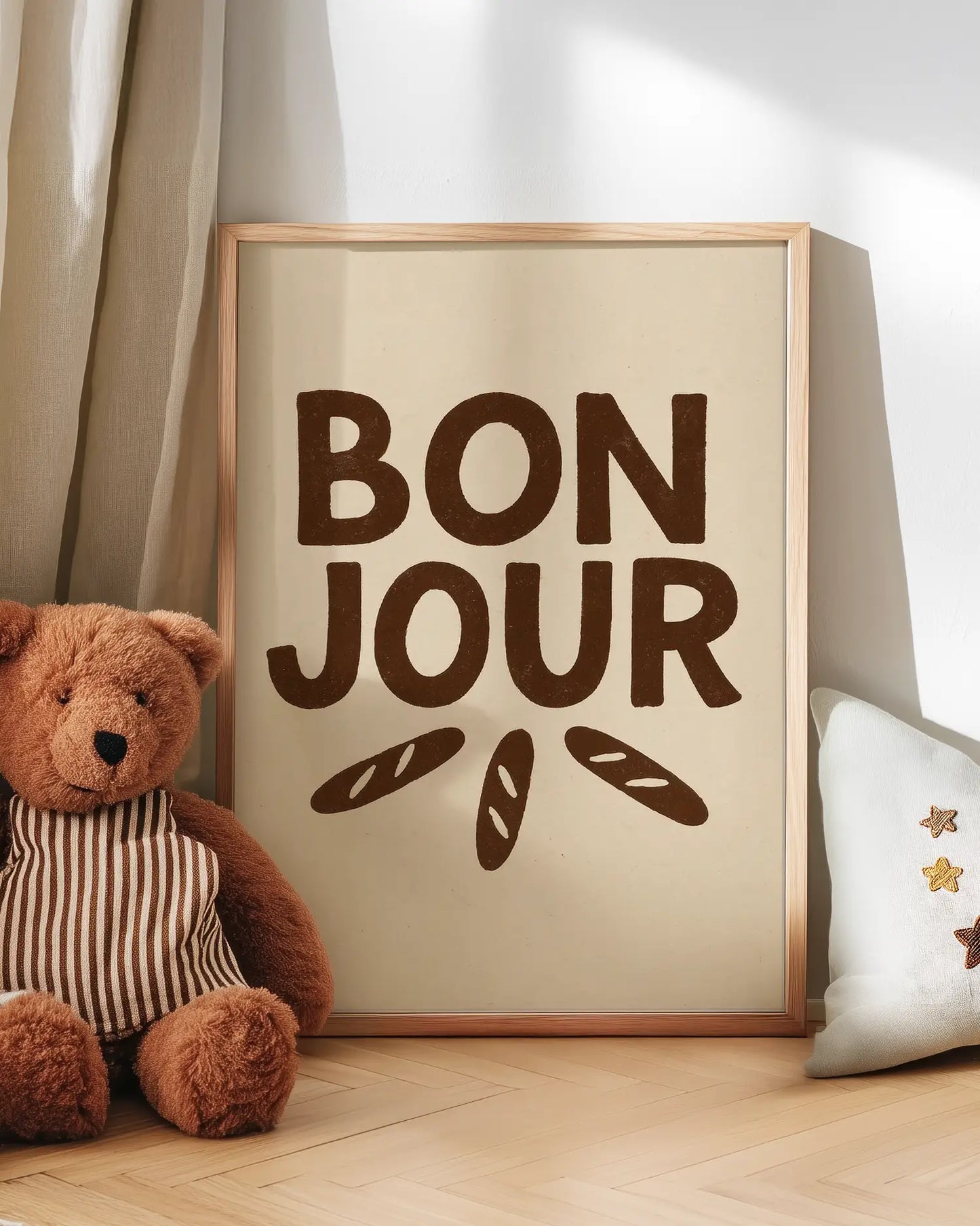 'Bonjour' poster with a teddy bear and decorative pillow on a wooden floor.