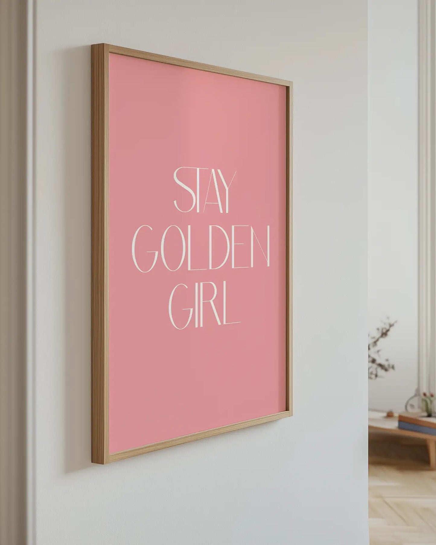 Pink framed poster with 'Stay Golden Girl' text on a white wall.