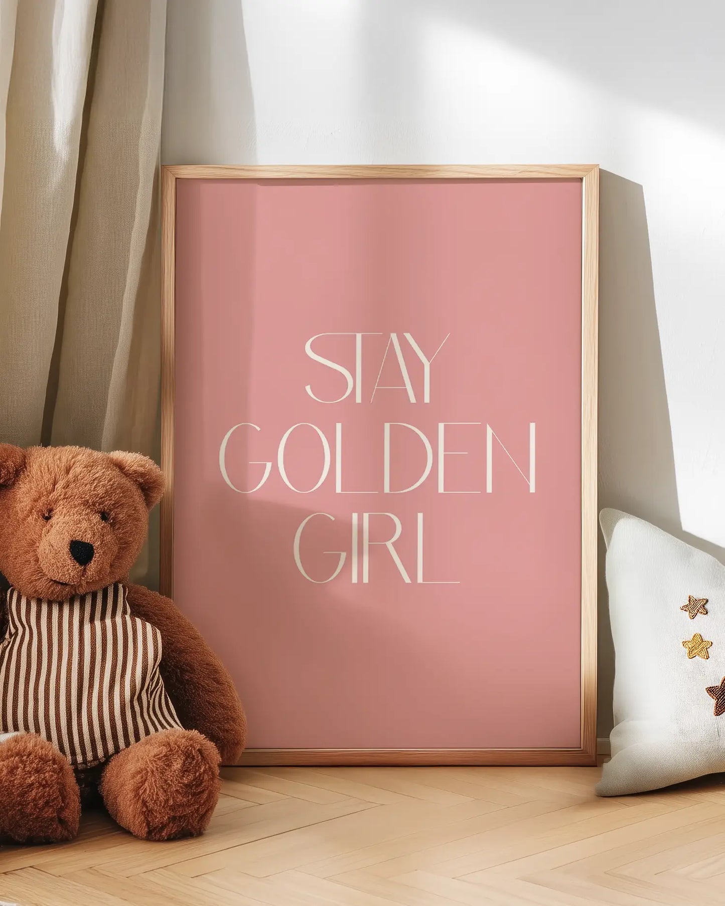 Pink poster with 'Stay Golden Girl' text next to a teddy bear and decorative pillow.