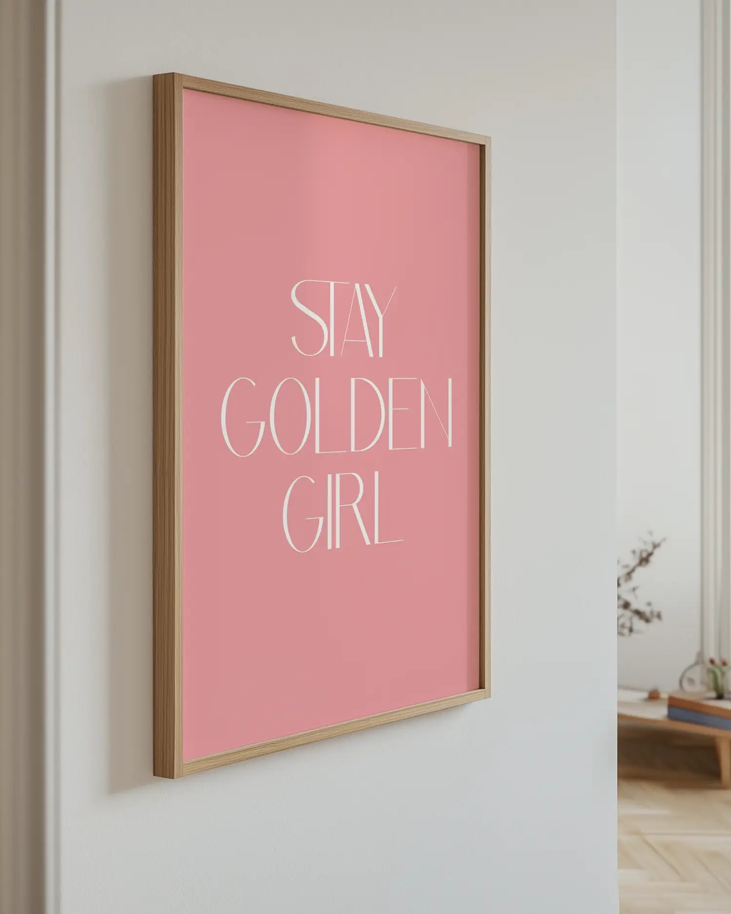 Pink framed poster with 'Stay Golden Girl' text on a white wall.